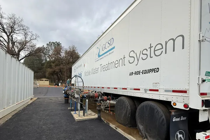 A mobile water treatment system mounted on a trailer with various hoses and equipment, set against a cloudy sky.