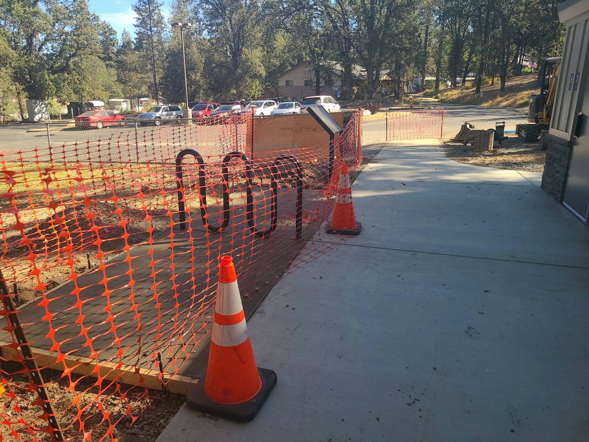 Construction site with orange safety netting, traffic cones, and a nearby parking lot.