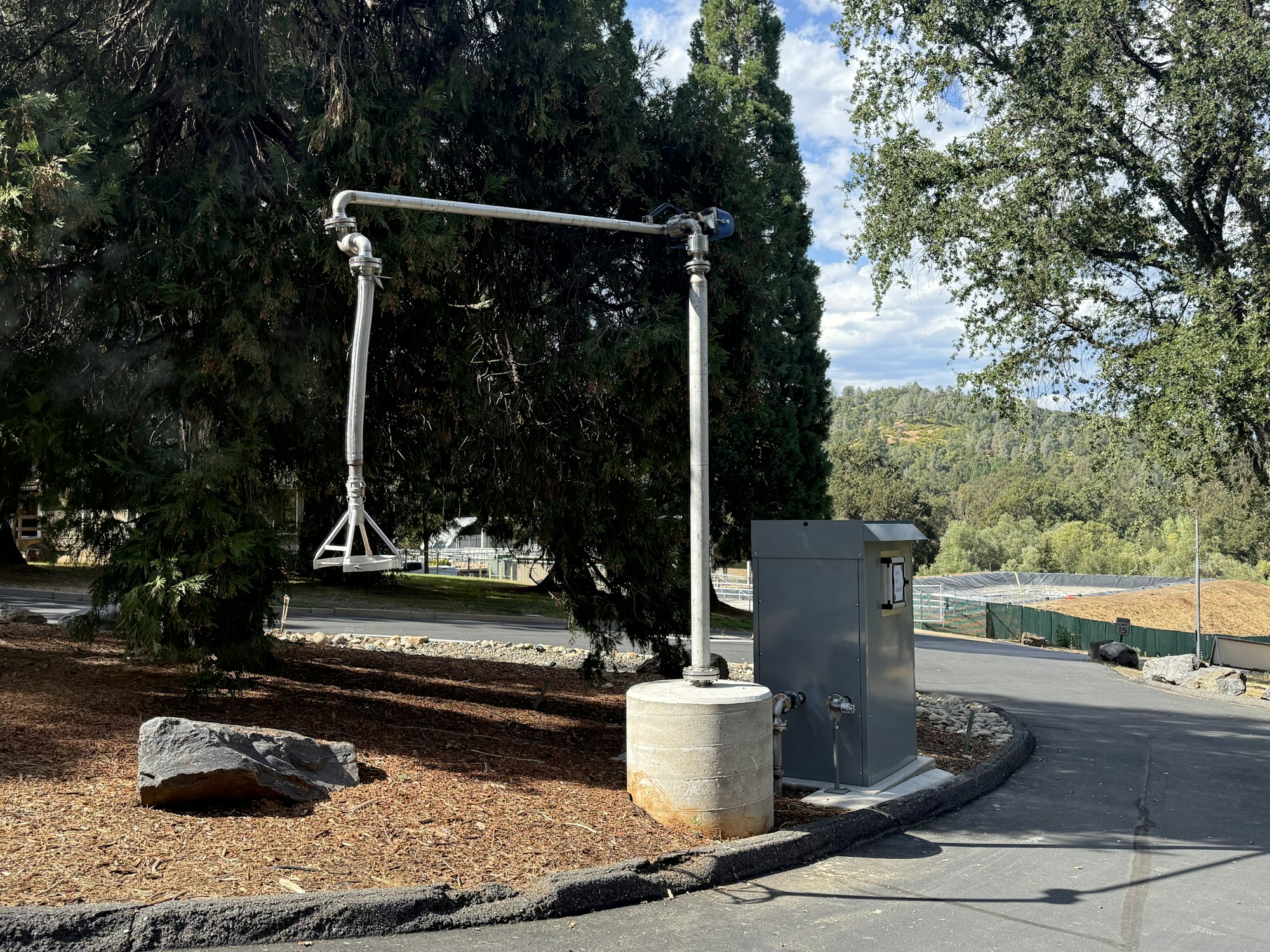Metal structure and control box on roadside, surrounded by trees and a rocky landscape.