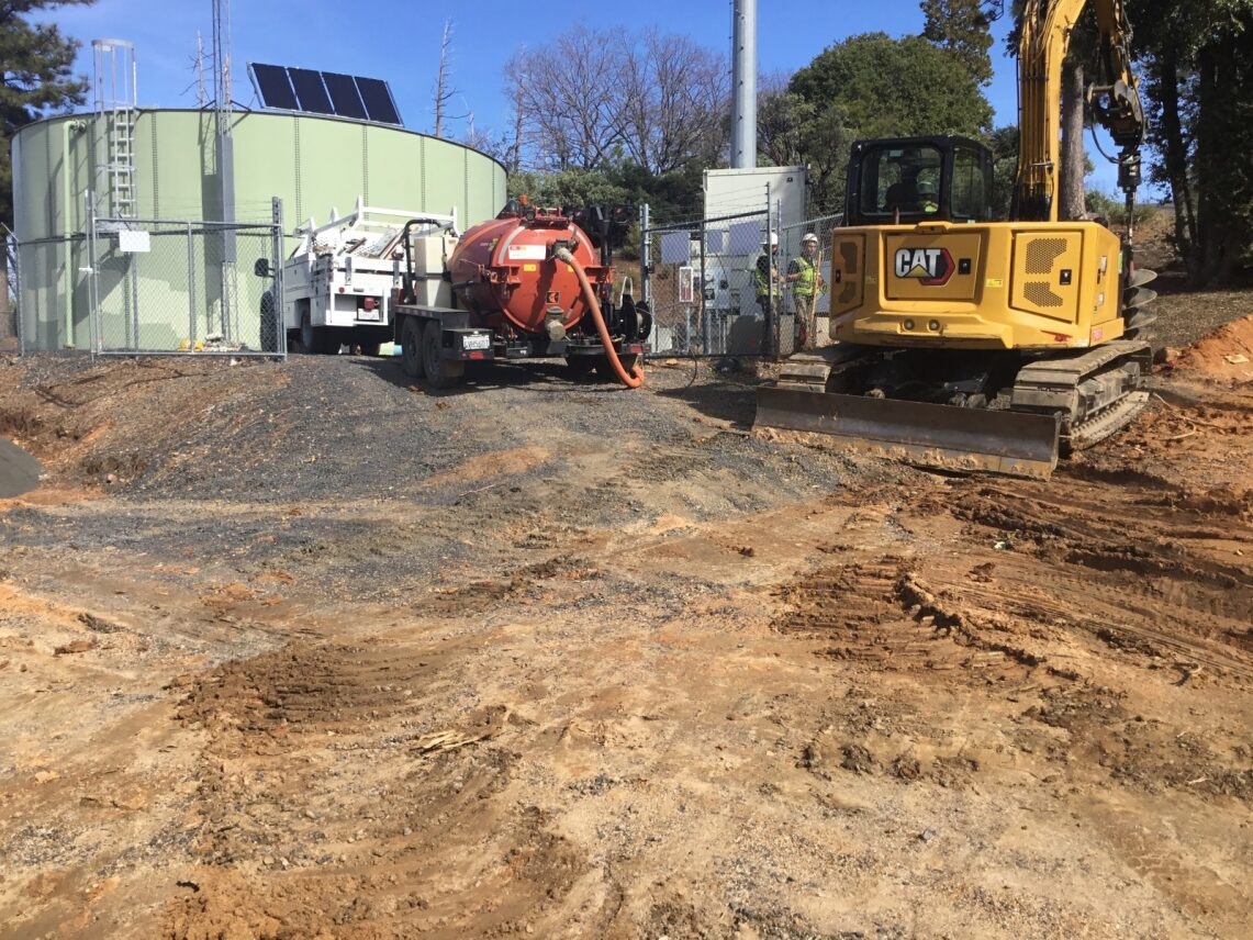 Construction site with an excavator, utility truck, and a green tank with solar panels.