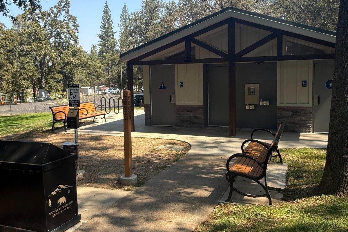 The image shows a restroom facility in a park, with benches, a trash can, and a pet waste station nearby.
