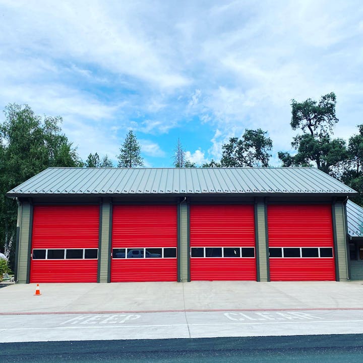 A building with four red garage doors under a blue sky with clouds.
