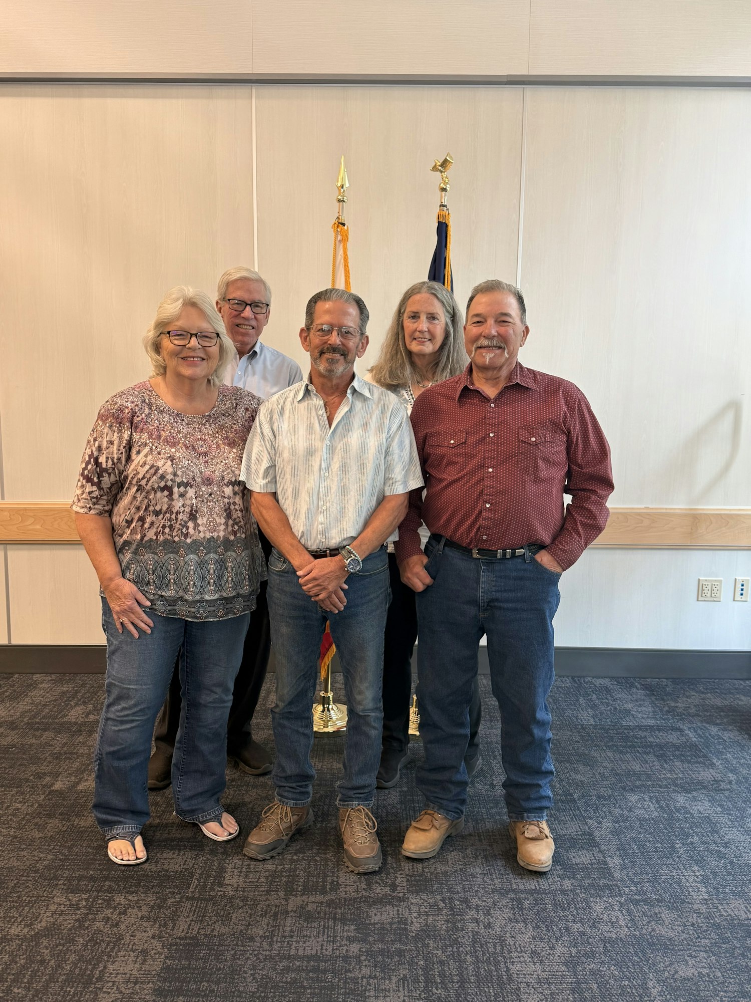 Five people standing in a room with flags in the background.