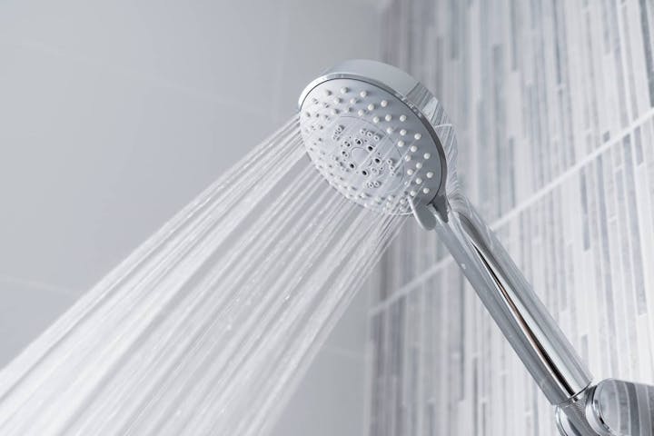 A showerhead spraying water in a tiled bathroom.