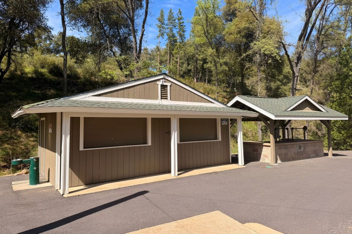 A building with a sloped roof, surrounded by trees, features covered areas and a paved walkway. It's likely a recreational facility.