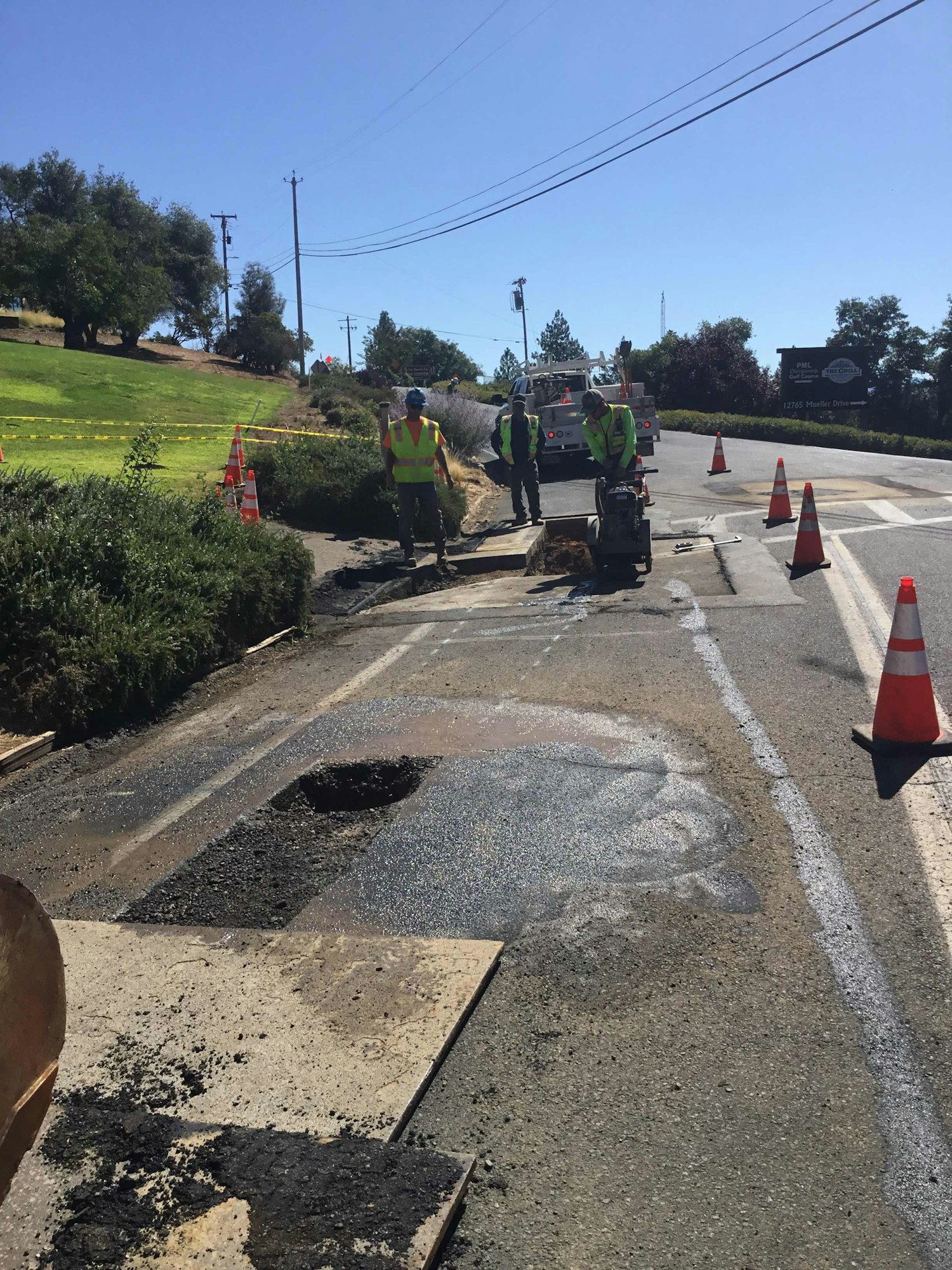 Roadwork scene: Workers in safety vests repair a road with traffic cones and machinery under clear skies.