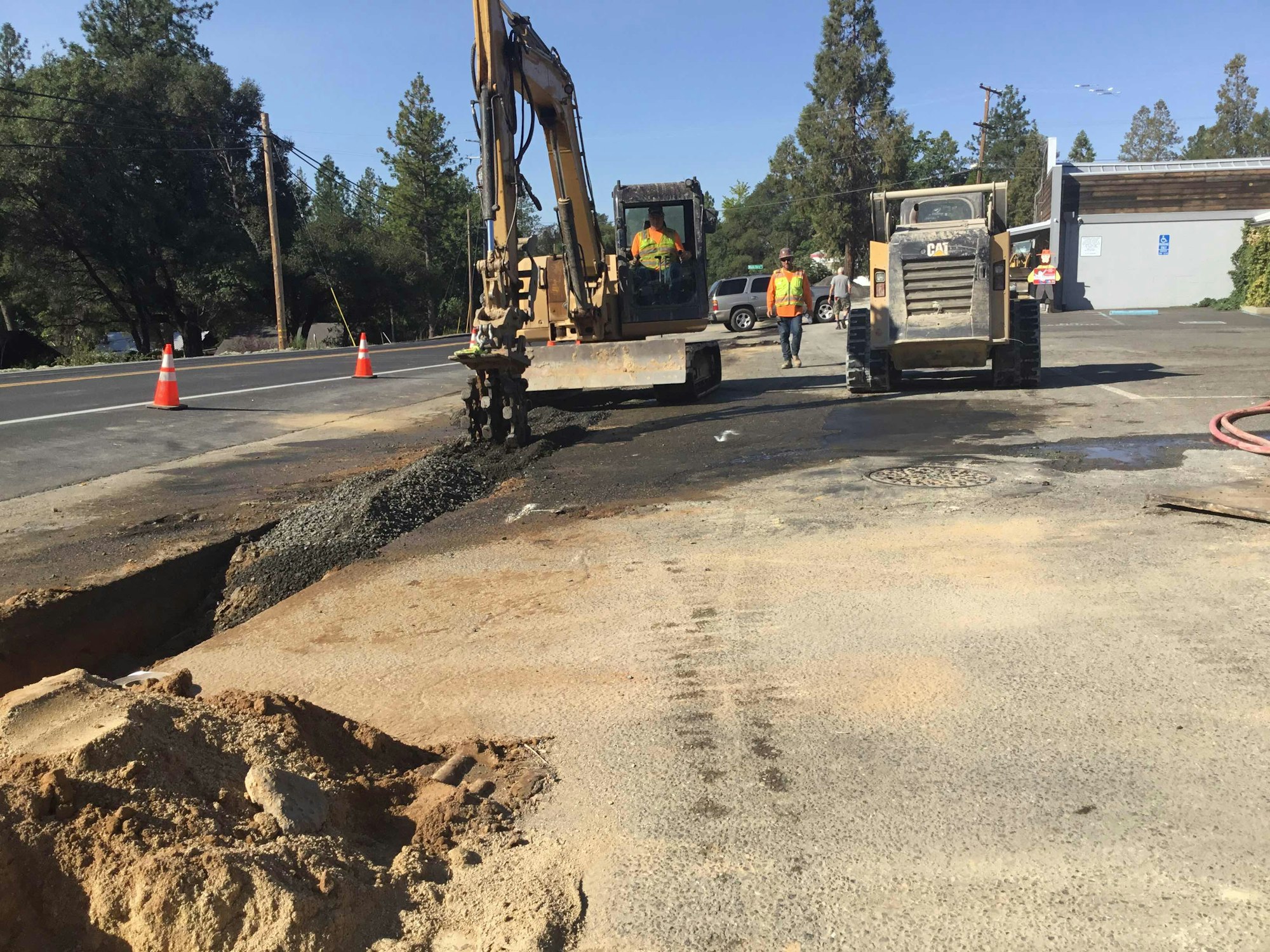 Construction site with machinery, workers in vests, and road cones beside a road.
