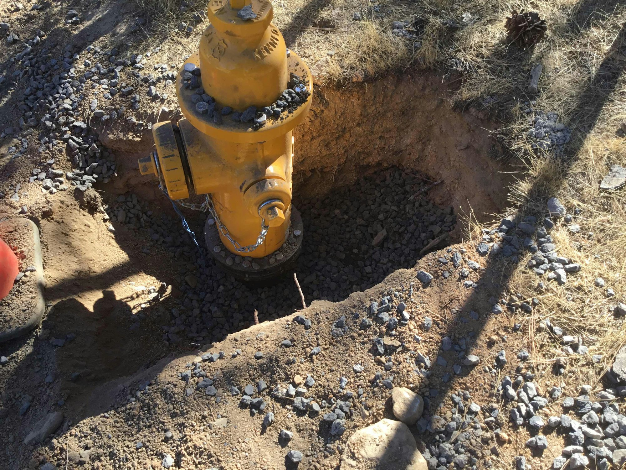 Yellow fire hydrant partially unearthed, surrounded by dirt and gravel.