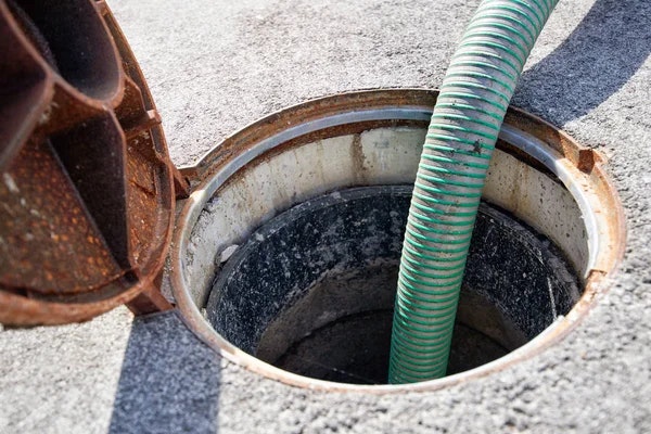 A green hose inserted into an open manhole on a concrete surface.