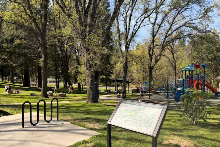 A community park with green grass, playground equipment, picnic areas, and visitors enjoying the outdoors.