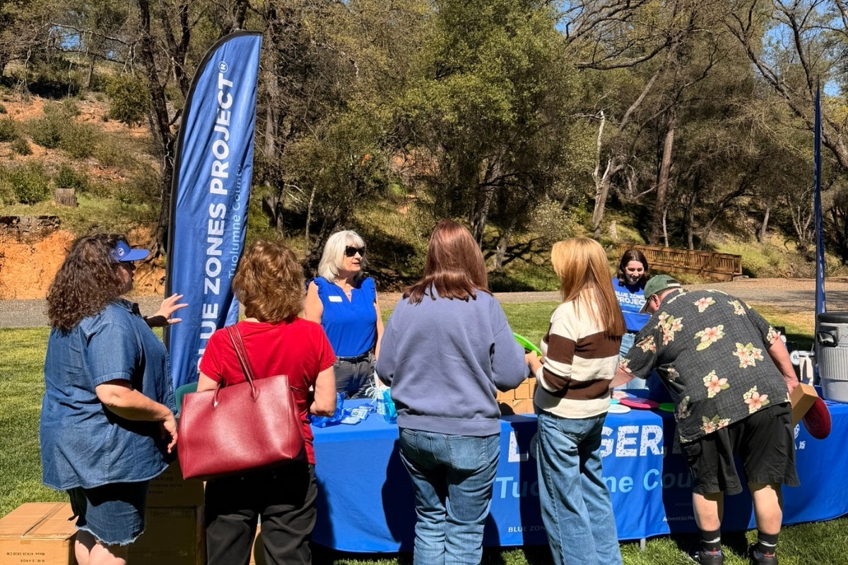 A group of people at an outdoor event visiting a booth for the Blue Zones Project, promoting healthy living and community engagement.