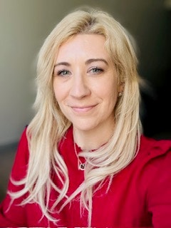 A person with long blonde hair wearing a red top, smiling softly.