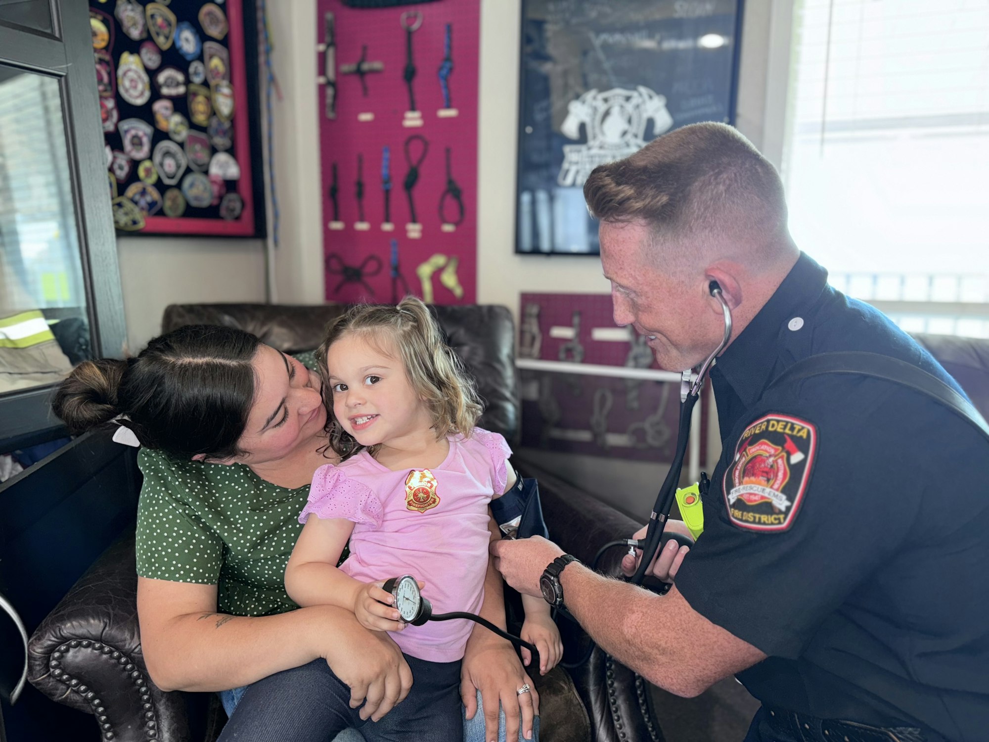 A firefighter is checking a child's blood pressure while the mother watches lovingly.