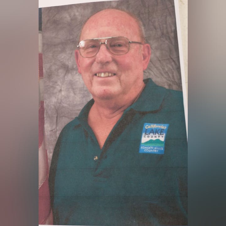 A smiling man with glasses wearing a shirt with a 'Lake County' badge.