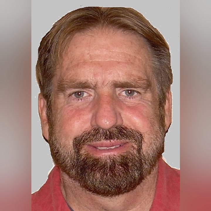 A man with a beard smiling against a white background.