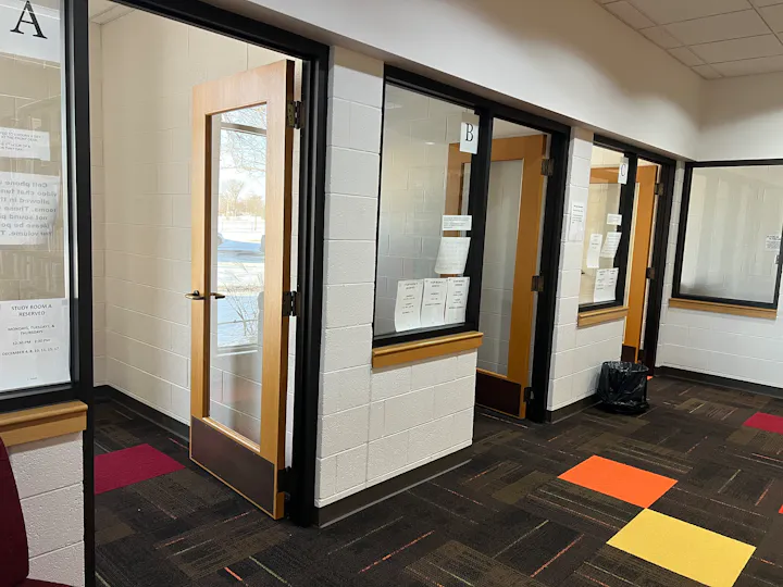 Glass-doored study rooms labeled A, B, and C, featuring colorful carpet tiles and reserved signs.