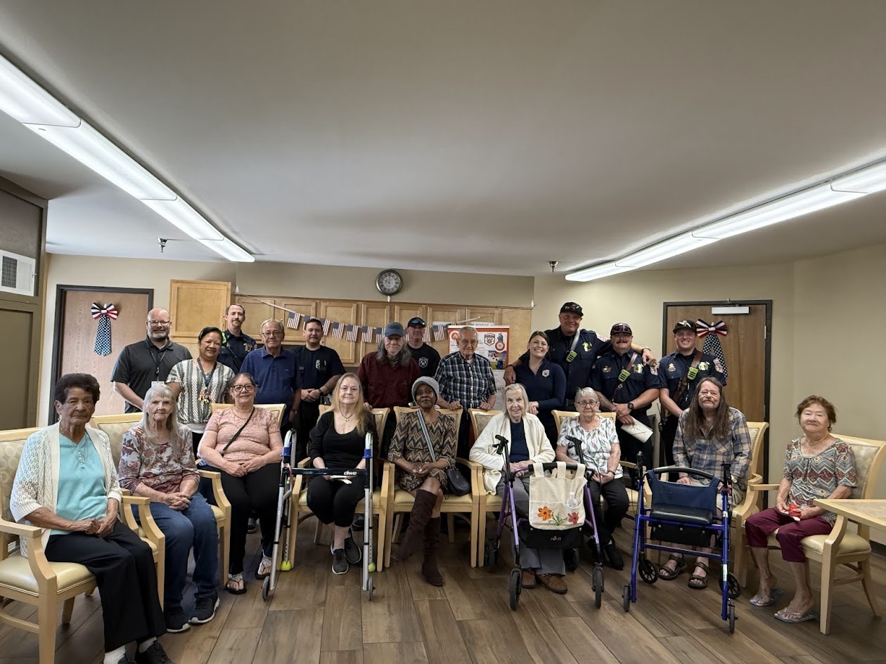 A group of people, including seniors and uniformed officers, are gathered in a room with chairs and decorations.