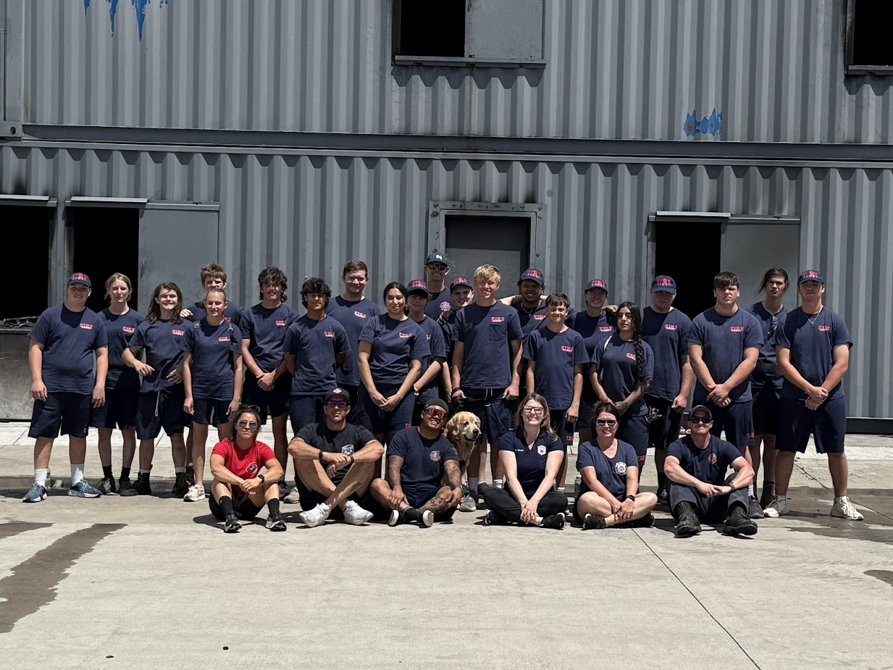 A group of people in matching uniforms pose outdoors in front of a large industrial building.