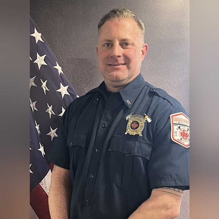 A man in a firefighter's uniform standing in front of an American flag.