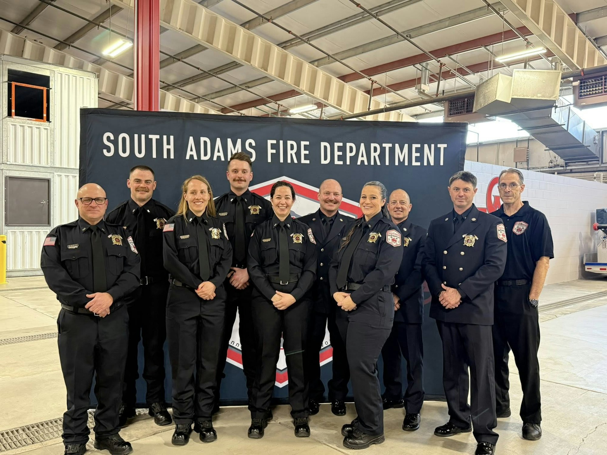 A group photo of firefighters from the South Adams Fire Department, standing in front of a banner in a fire station.