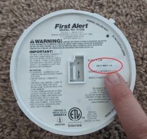 A hand pointing at a "DO NOT PAINT" label on the back of a First Alert smoke detector.