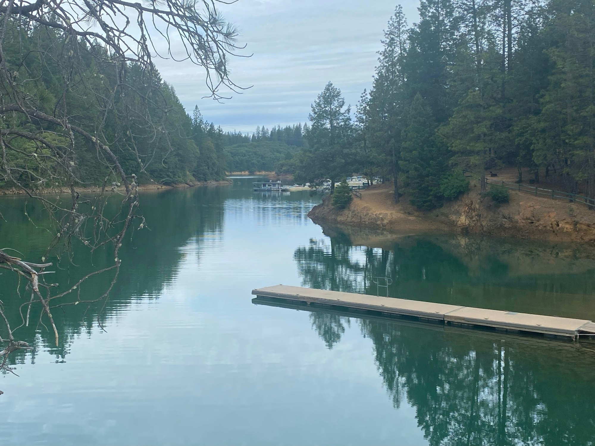 A serene lake with trees, a jetty, and reflections on the water.