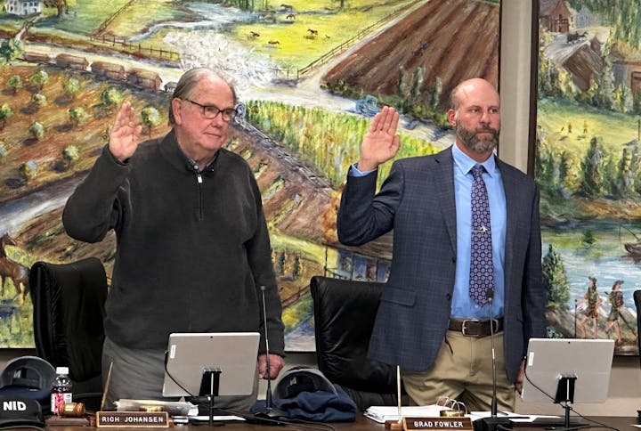 Two men standing with hands raised, taking an oath in front of a painted landscape mural.