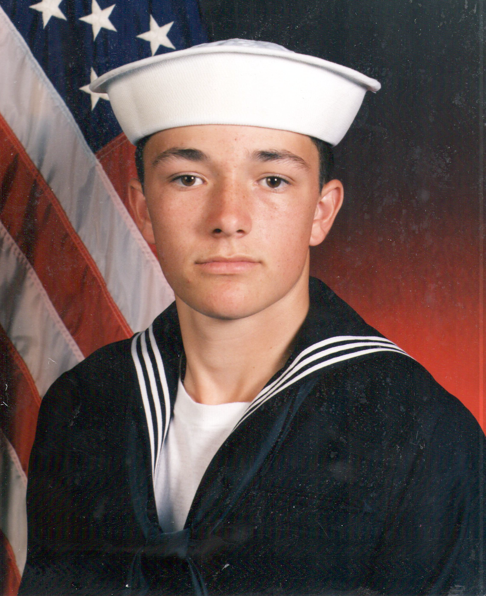 A young person wearing a sailor uniform with an American flag background.
