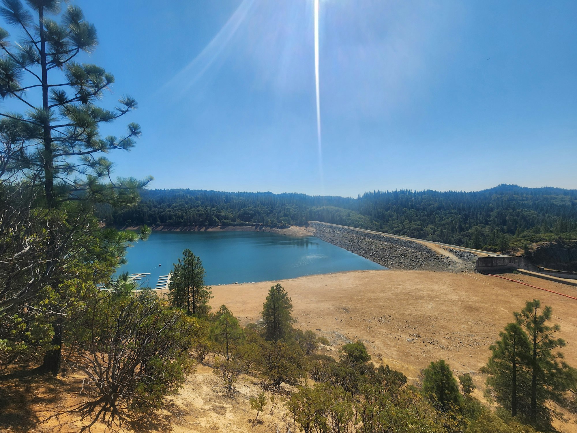 A scenic view with a reservoir, a dam, trees, and a clear blue sky.