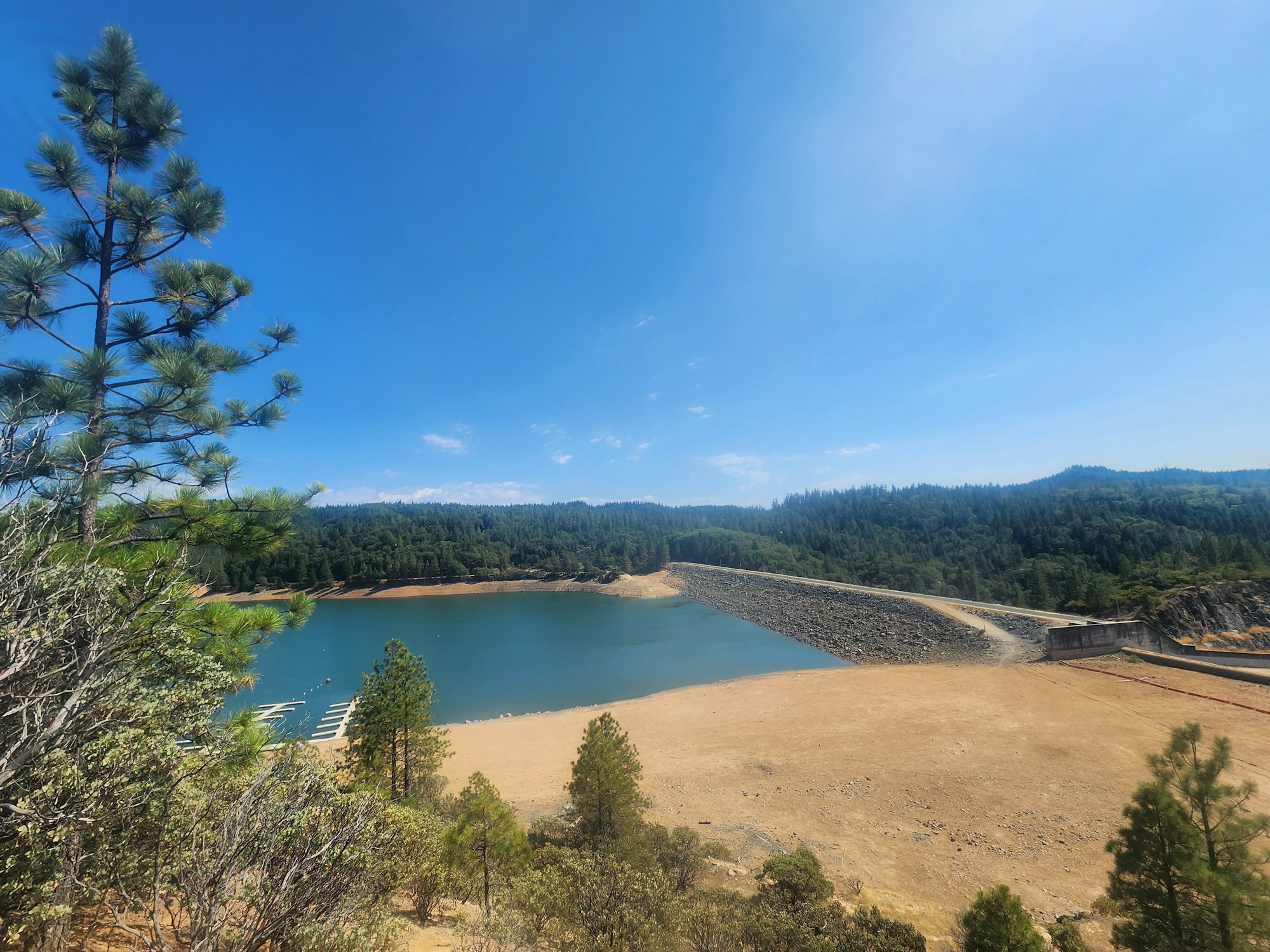 A scenic view of a lake, trees, a dam, and clear skies.