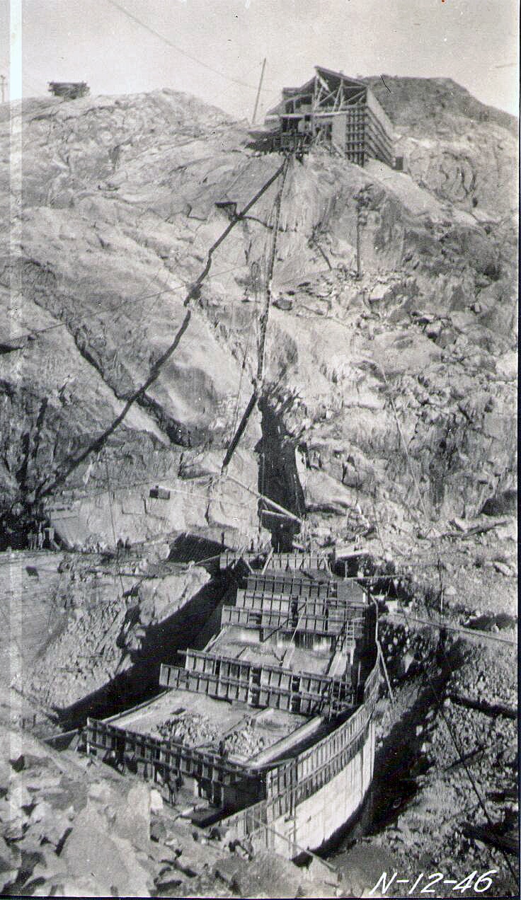 Construction site on rocky terrain, with scaffolding, machinery, and a structure at the top of a cliff.