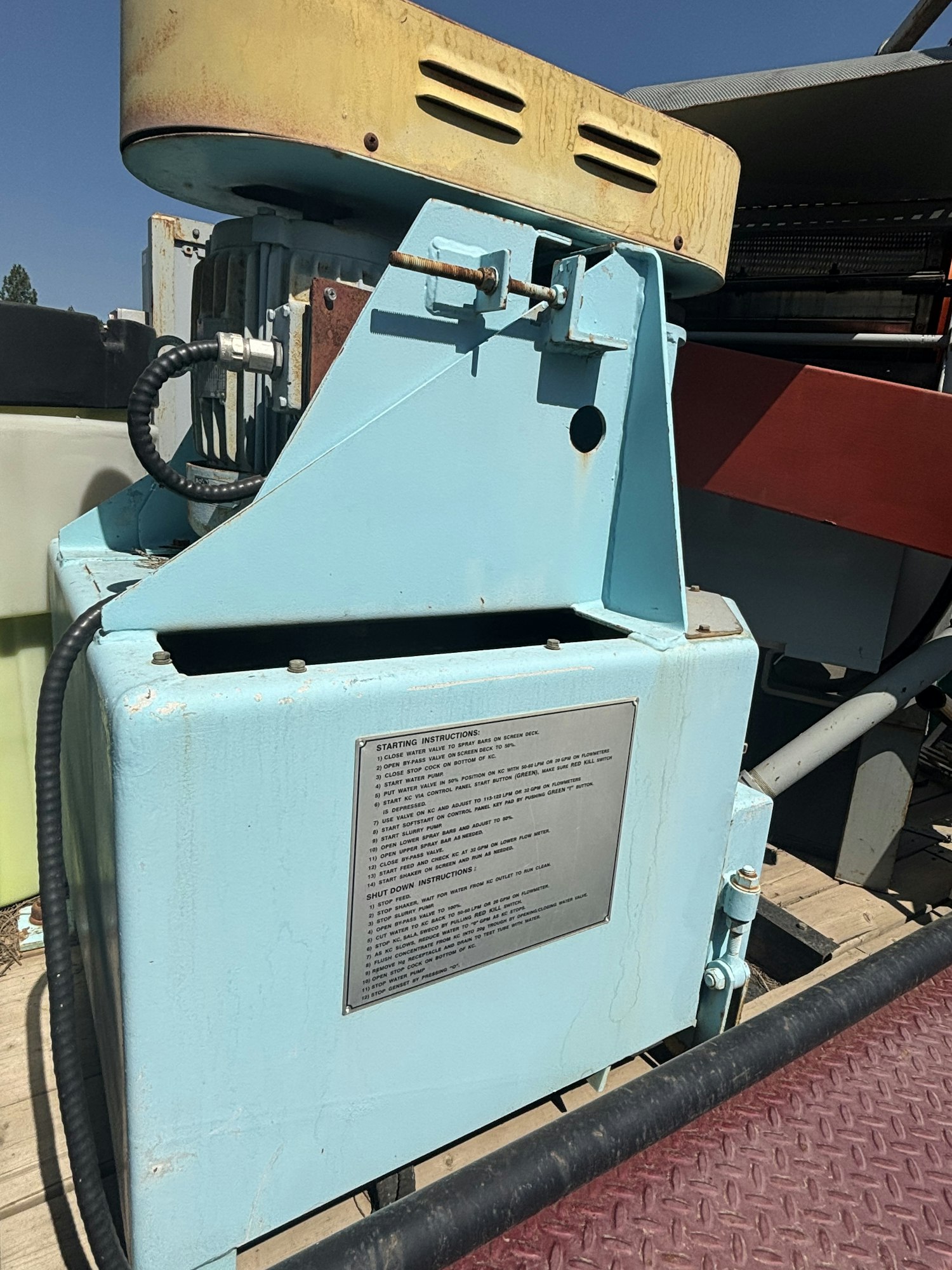 The image shows a blue industrial machine with a yellow top and an instruction plate detailing starting and shutdown procedures.