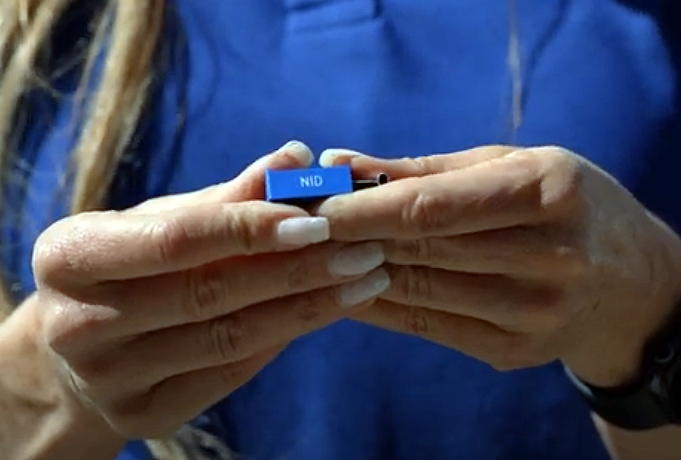 A person in a blue shirt holds a small blue item labeled "NID" with both hands.