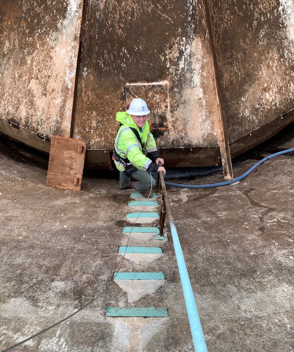 Person in safety gear climbing a ladder, with a large rusty structure in the background.