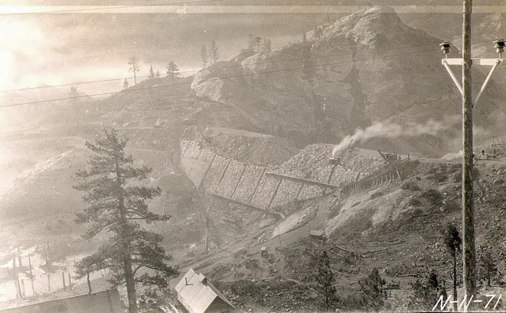 An old black-and-white photo showing a mountainous landscape with mining activities, machinery, and trees.