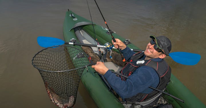Man fishing from his kayak with a fish in his net.