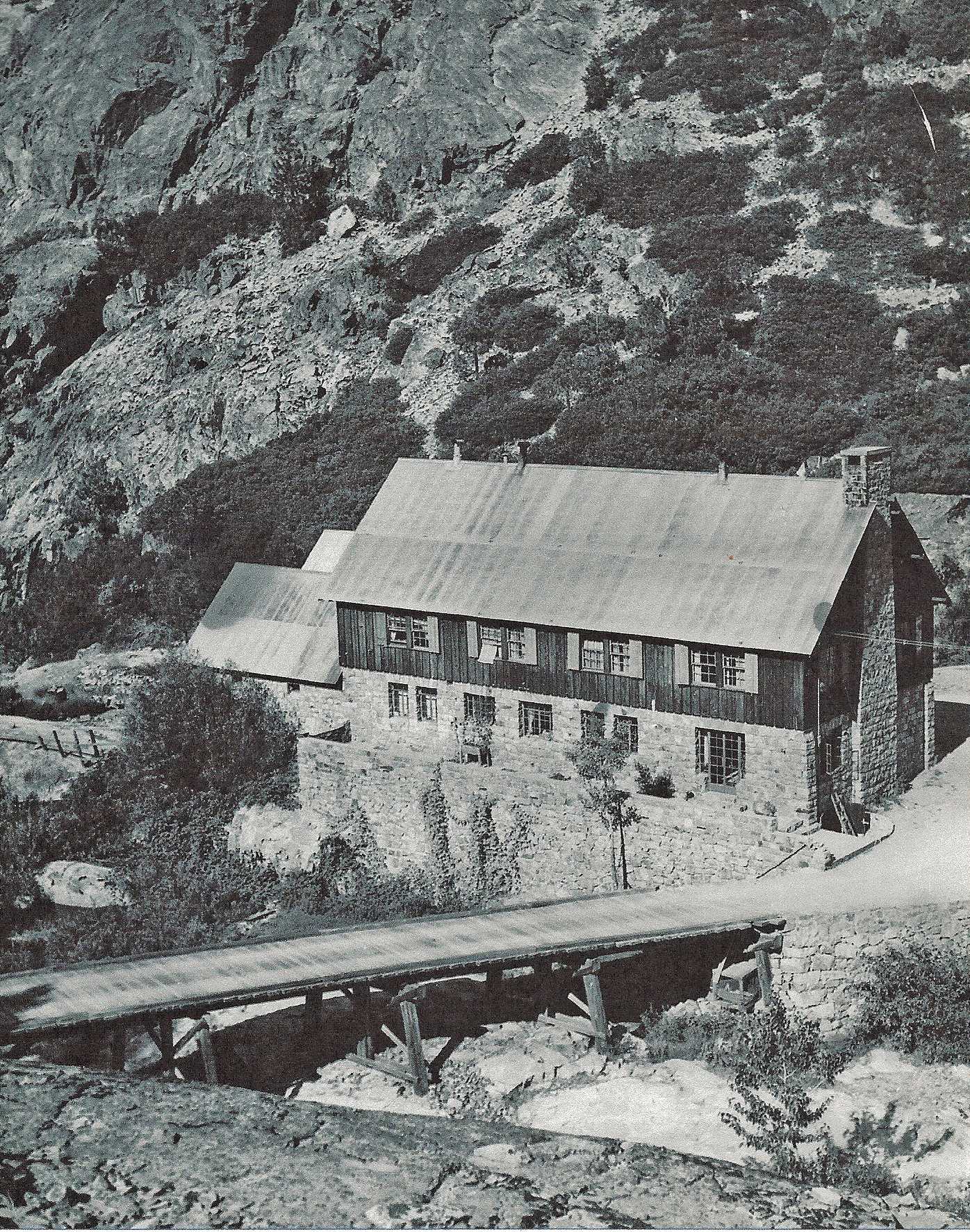 A rustic building with a wooden and stone structure, located in a mountainous area with trees and rocky landscape.