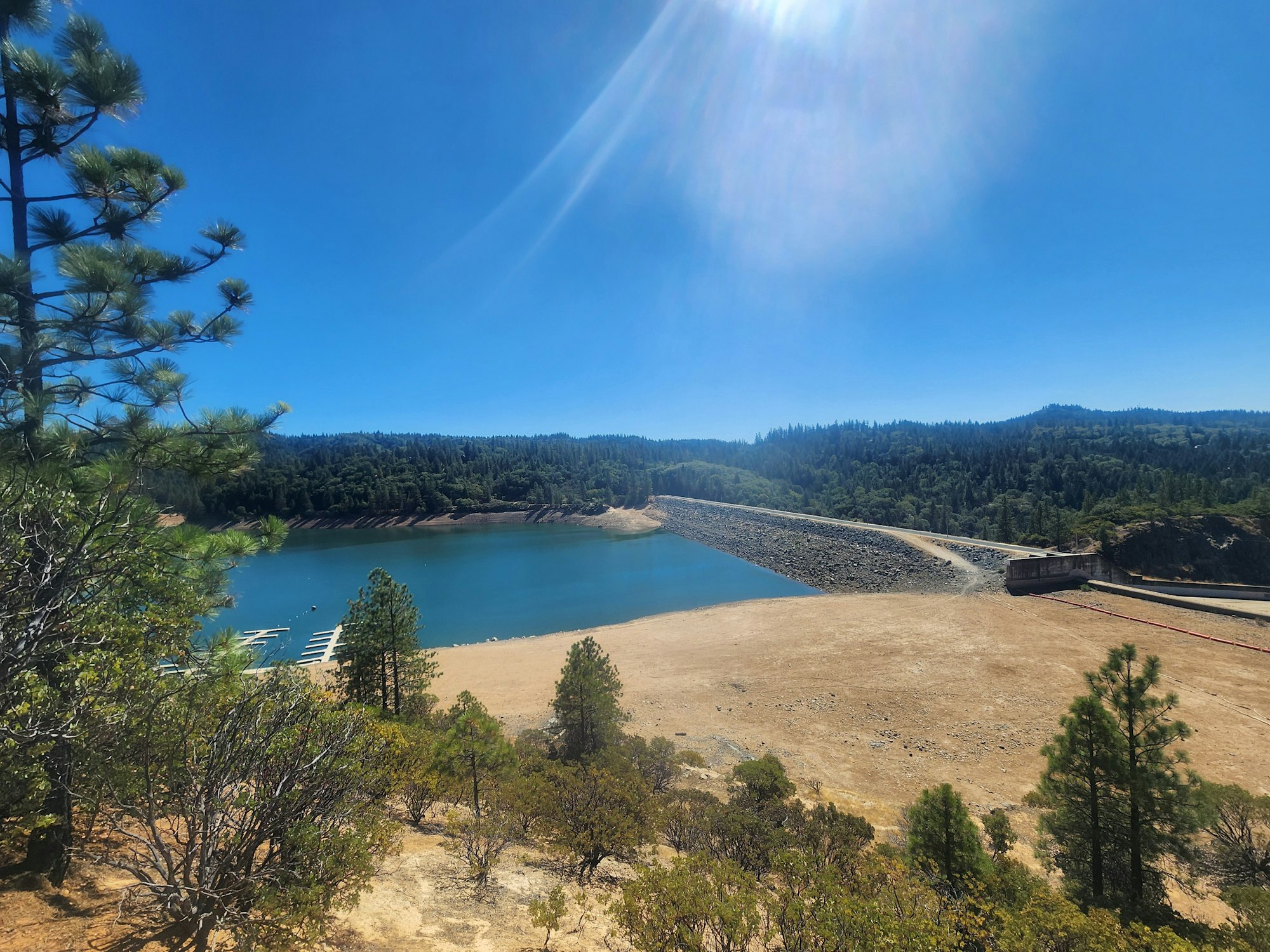 Reservoir surrounded by trees with a dam under a clear blue sky.