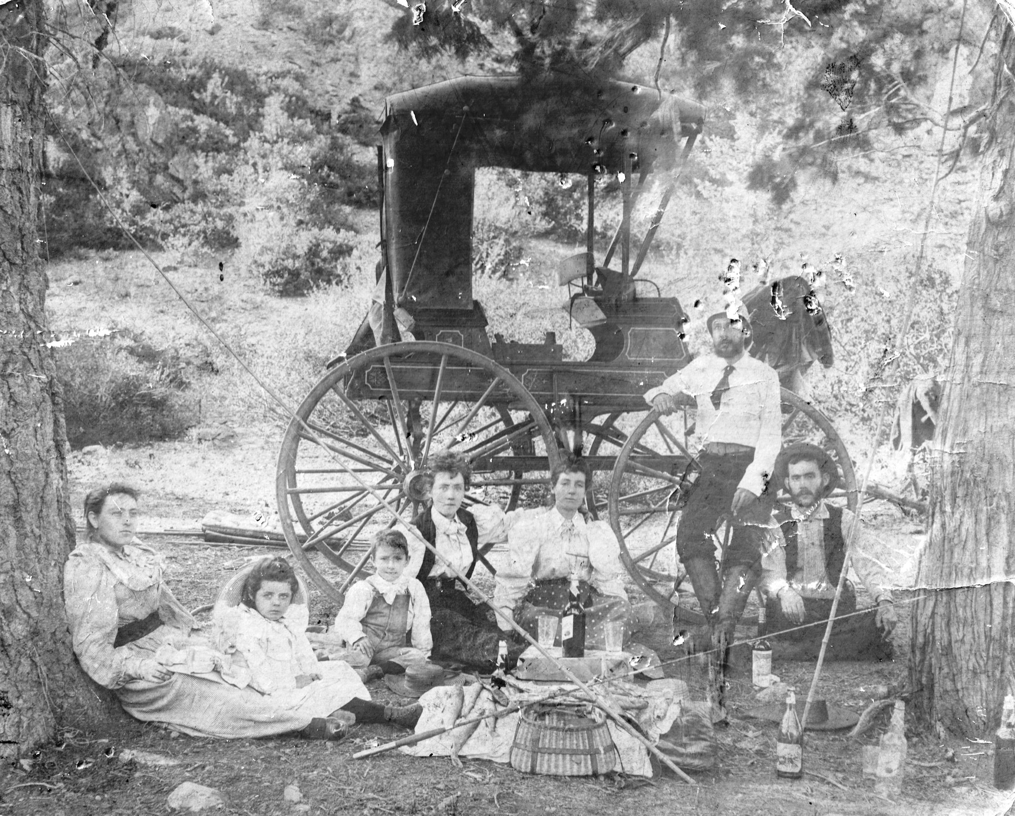 A vintage black-and-white photo of a group, including adults and children, gathered near a horse-drawn carriage outdoors.
