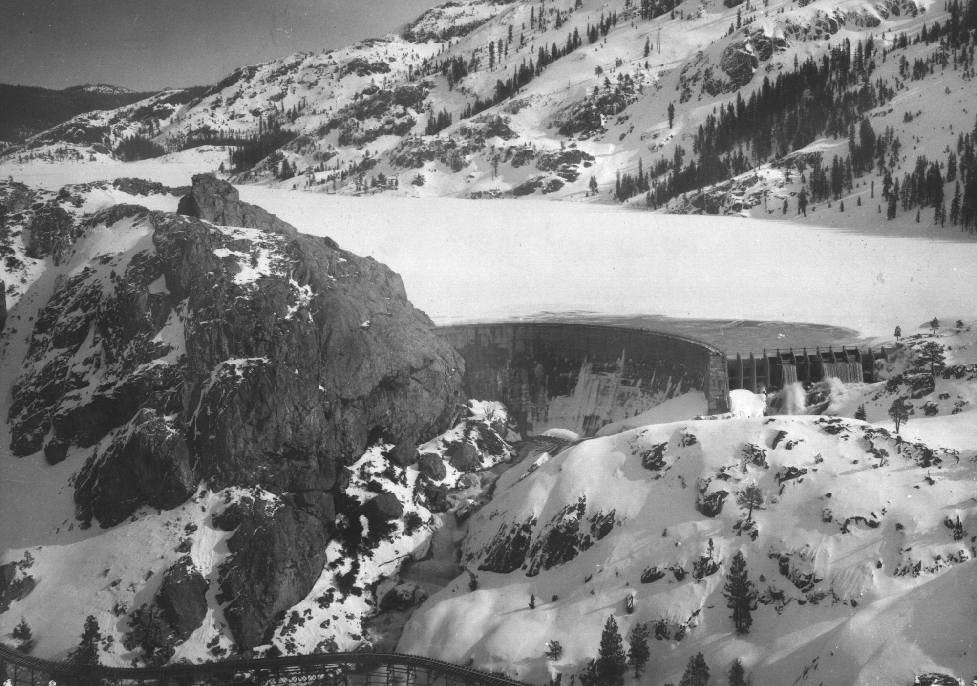 Snow-covered mountainous landscape with a large dam and rocky cliffs.