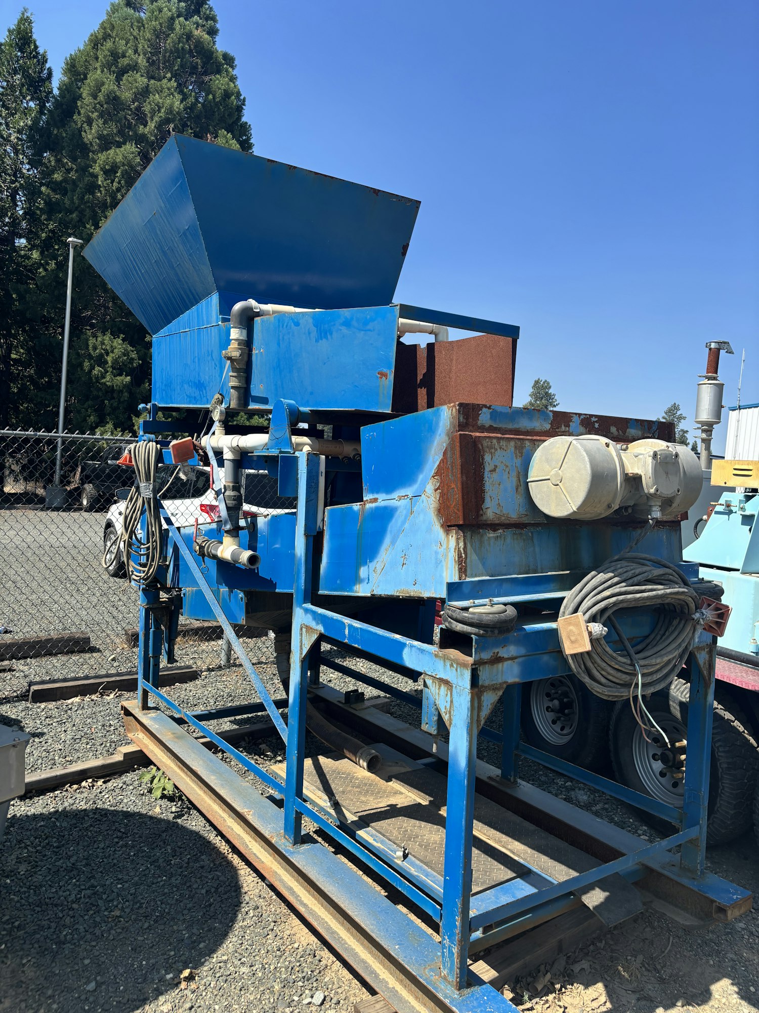 The image shows a large blue industrial machine, likely for processing materials, with a hopper and various components.