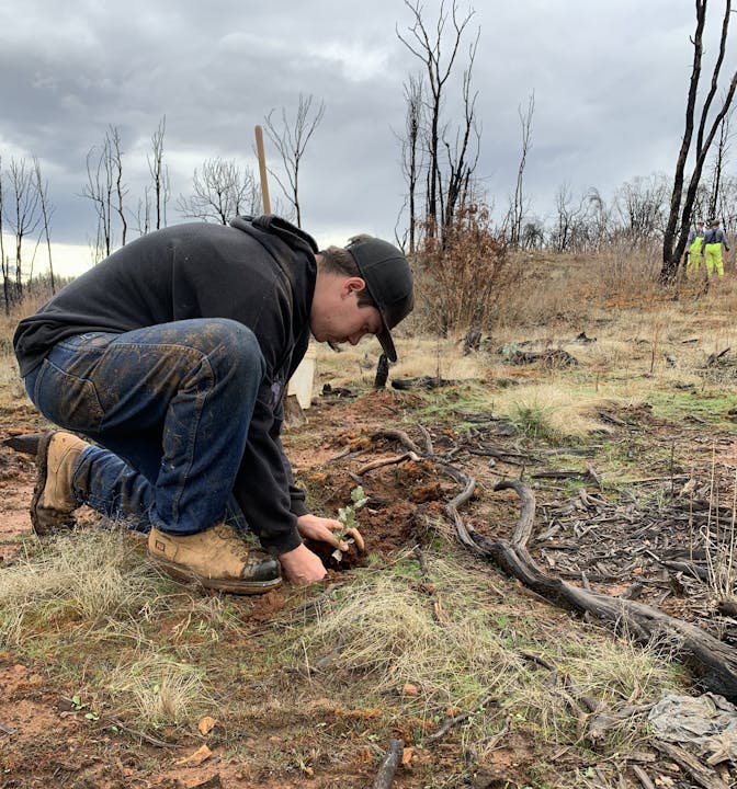 May contain: soil, clothing, pants, photography, plant, tree, hat, adult, male, man, person, wood, baseball cap, cap, vegetation, footwear, shoe, land, nature, outdoors, wilderness, jeans, face, head, and portrait
