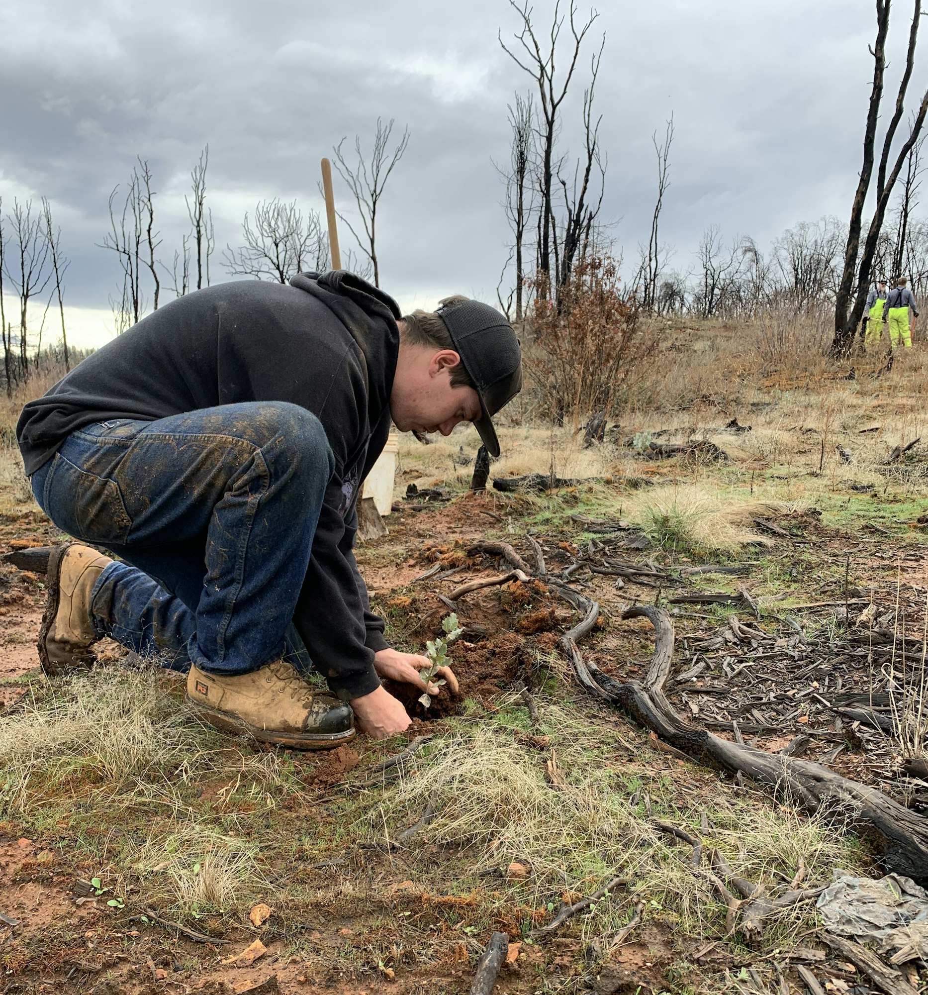 May contain: soil, clothing, pants, photography, plant, tree, hat, adult, male, man, person, wood, baseball cap, cap, vegetation, footwear, shoe, land, nature, outdoors, wilderness, jeans, face, head, and portrait