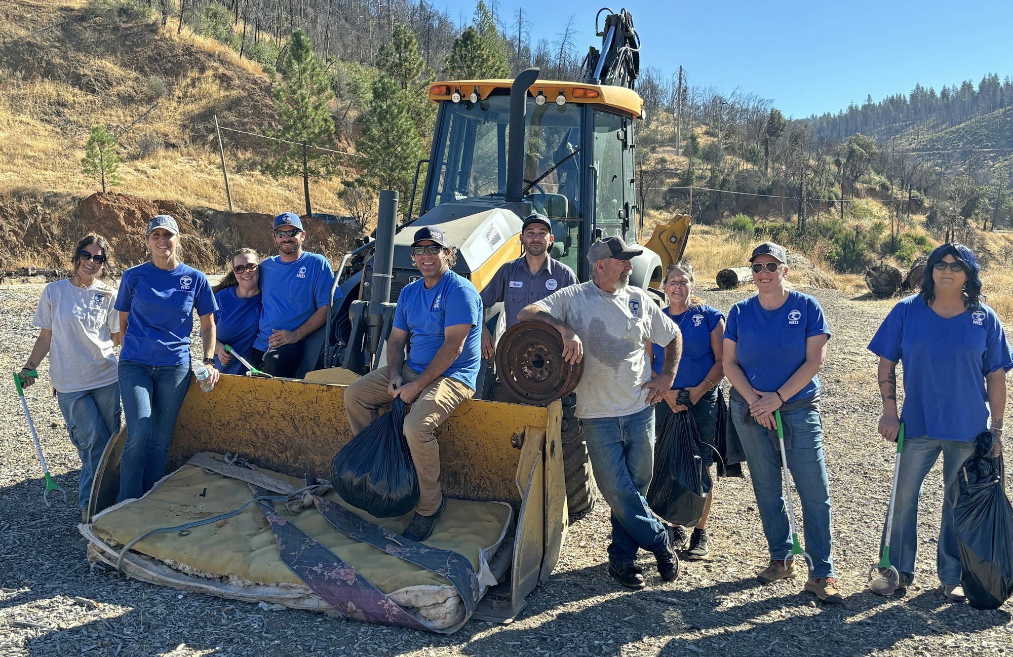 A group of people in blue shirts posing with a tractor, participating in a cleanup effort outdoors.