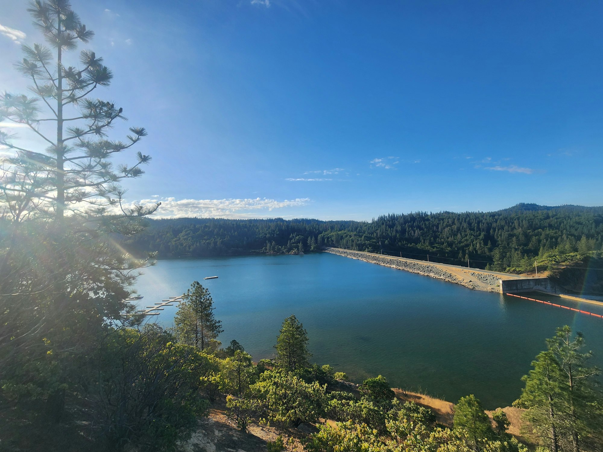 A scenic view of a reservoir with trees, clear skies, and a dam in the distance.