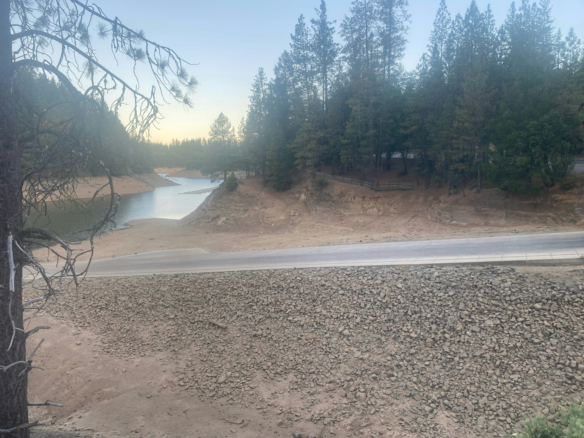 A serene landscape with a lake, surrounded by trees and a rocky shore, with a road in the foreground.