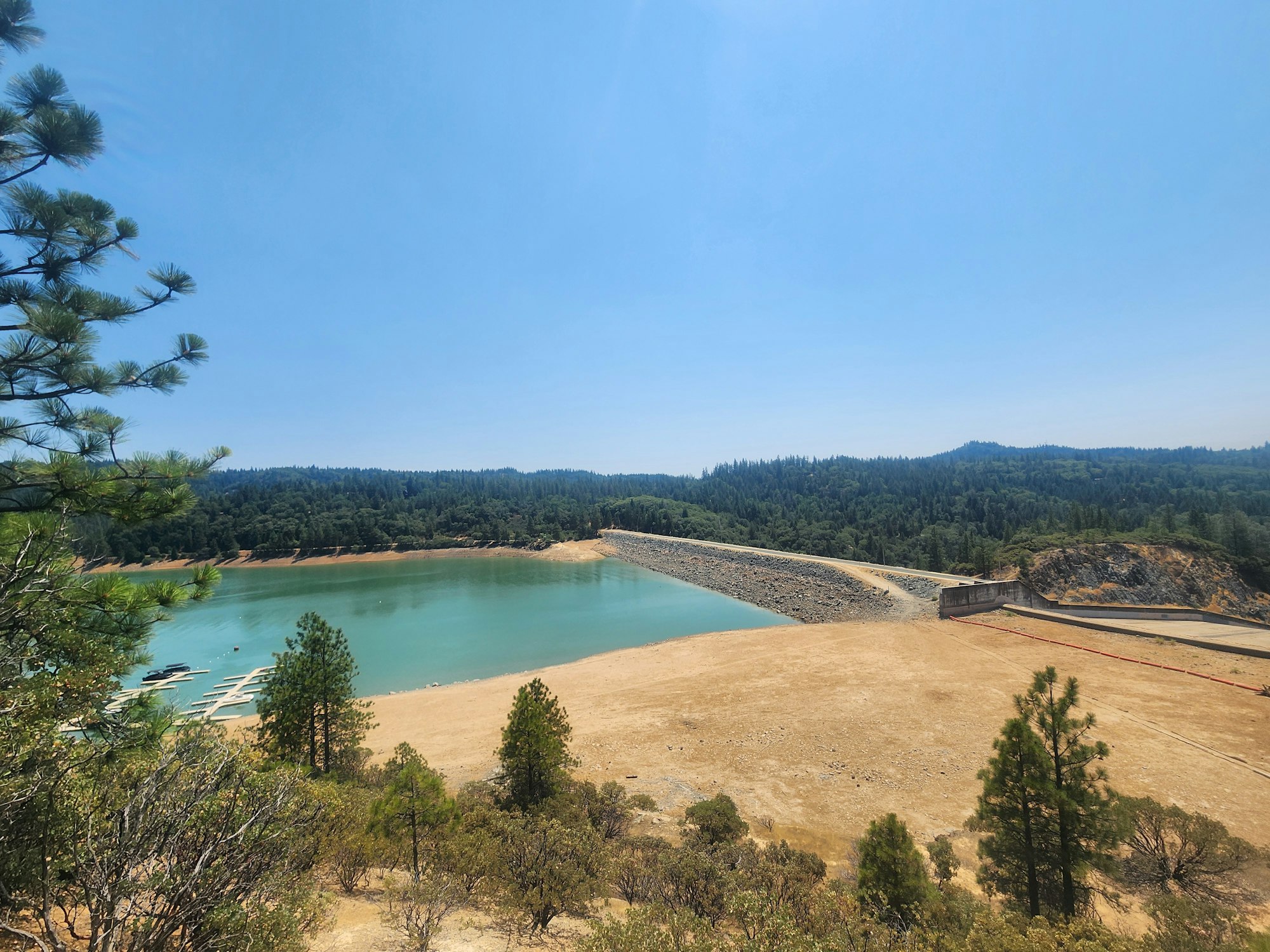A scenic reservoir surrounded by dry grassland and trees with a clear blue sky.