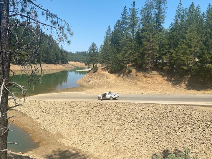 A serene landscape with a road, trees, and a lowered water level in a reservoir.