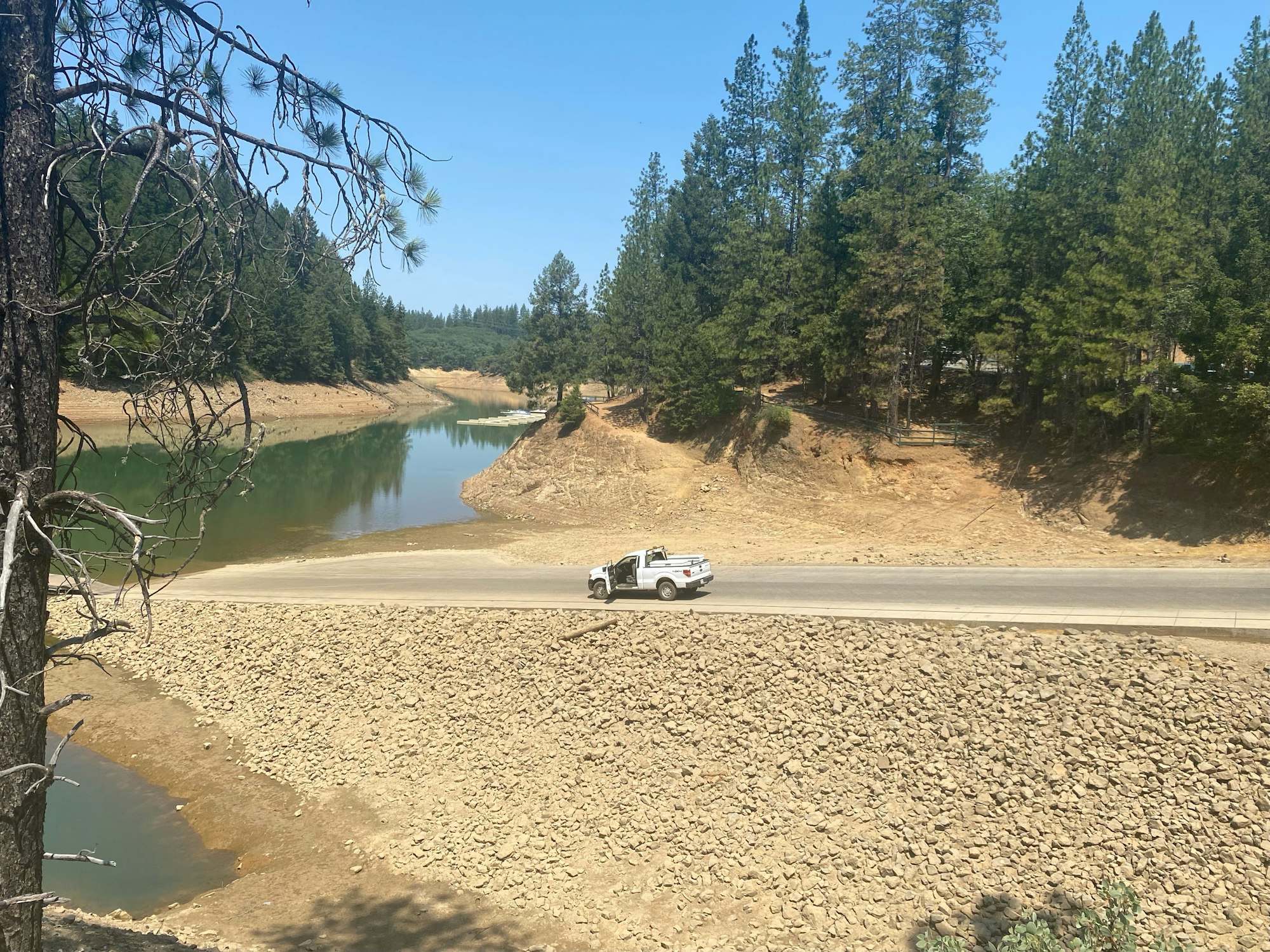 A serene landscape with a road, trees, and a lowered water level in a reservoir.