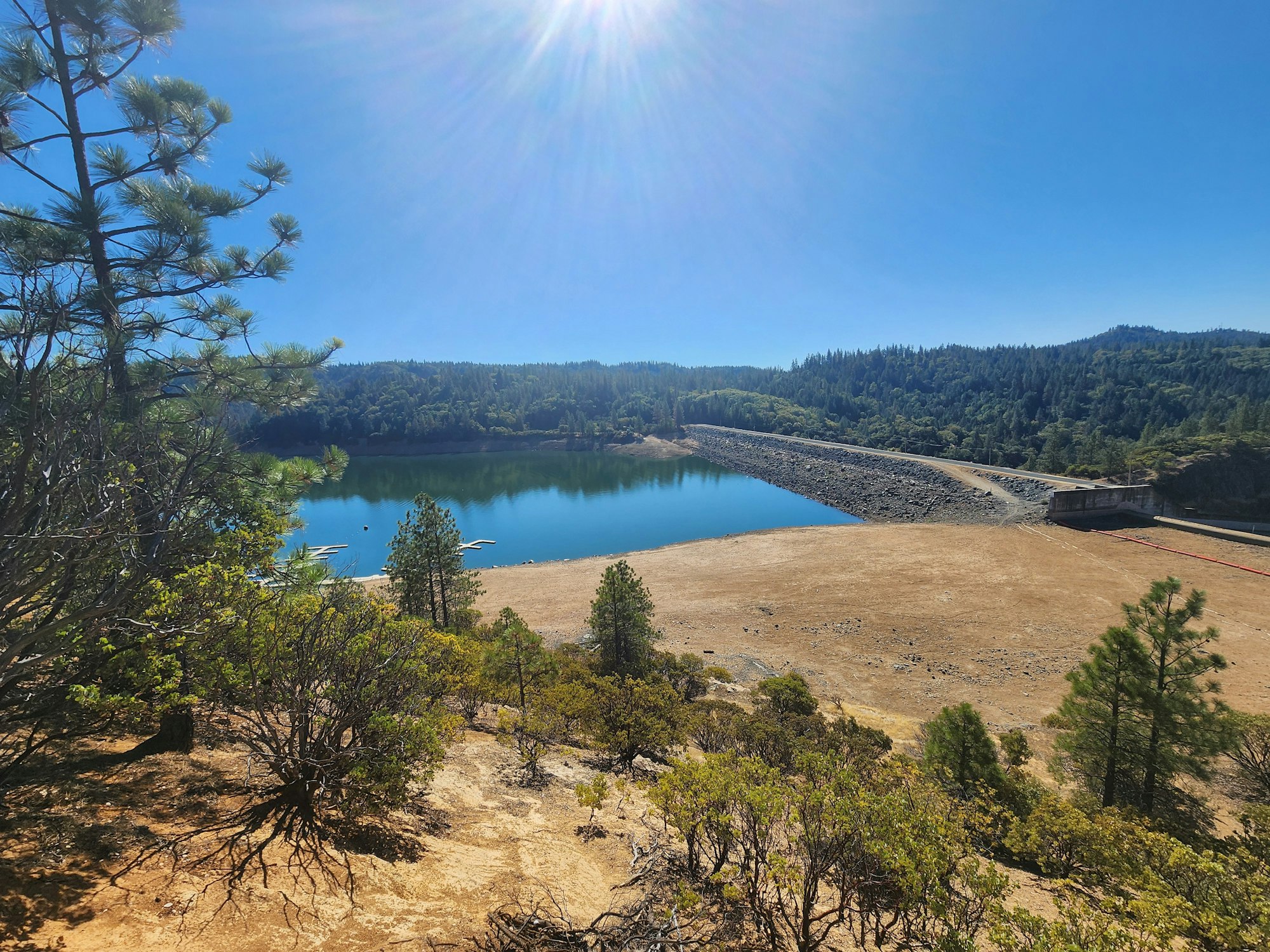 Sunny view of a reservoir with surrounding forest and a clear blue sky.